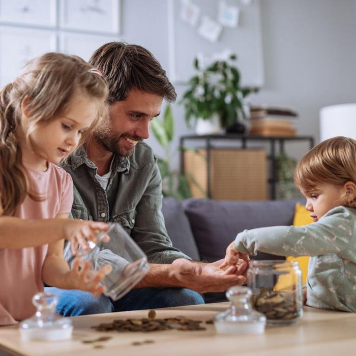 A father smiles as a preschooler and her younger brother count pennies from their money jars.