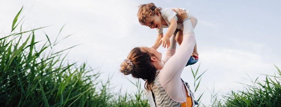 A young mom holds her giggling baby up in the air.